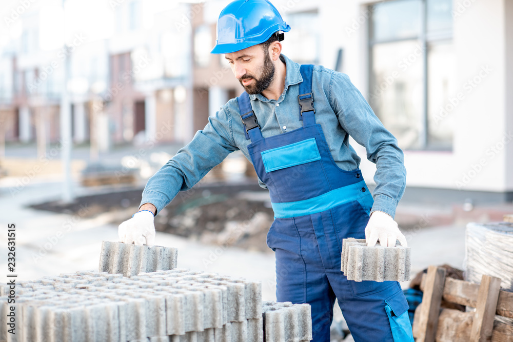 穿着制服的建筑工人从户外施工现场的托盘上取下铺路砖