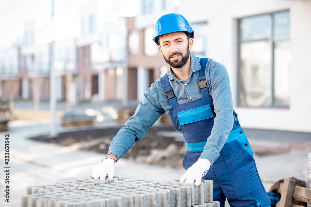 穿着制服的建筑工人从户外施工现场的托盘上取下铺路砖