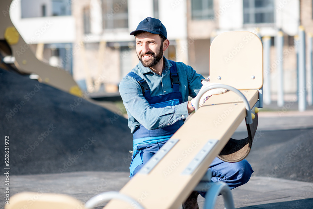 Handsome workman in uniform mounting kids swing on the playground outdoors