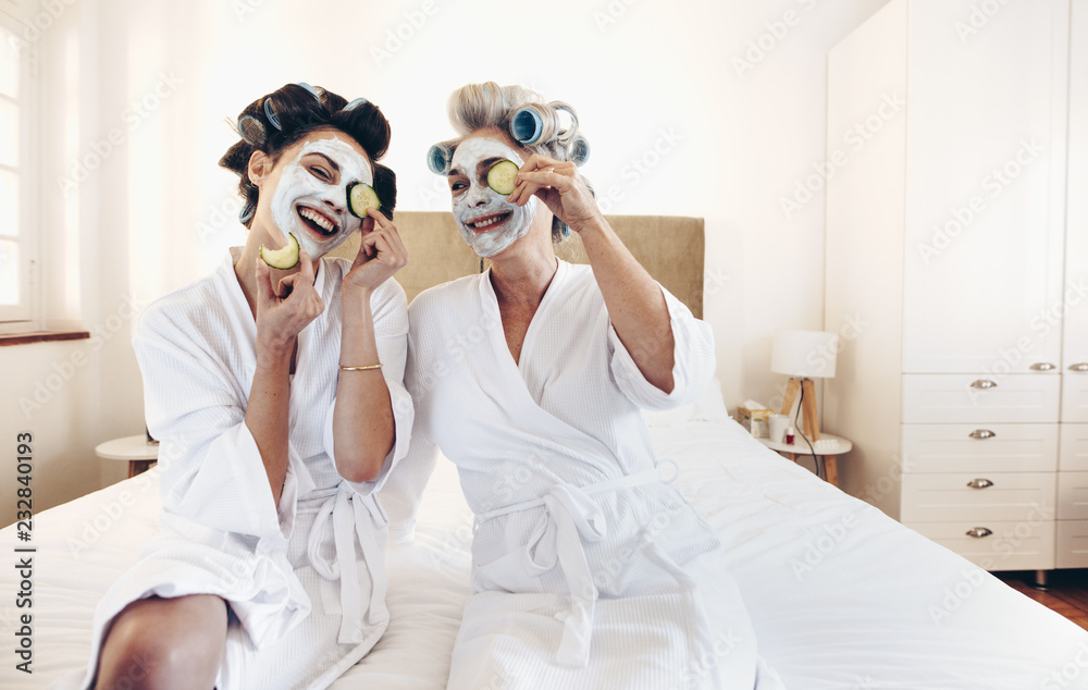 Happy women wearing beauty face pack sitting on bed holding slic