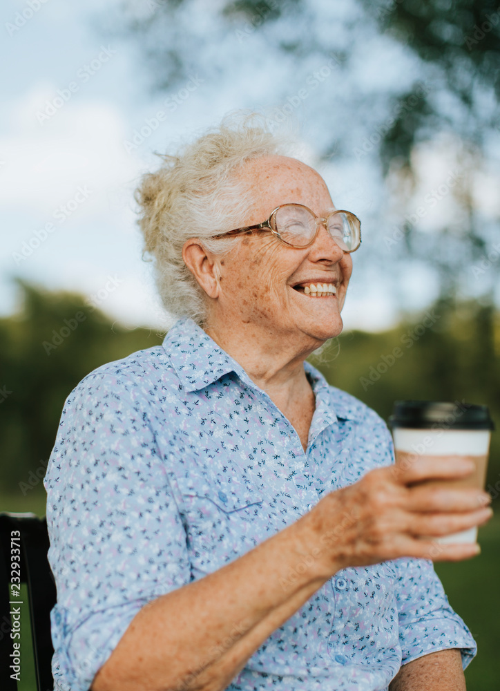 Happy senior woman having a takeaway coffee at the park