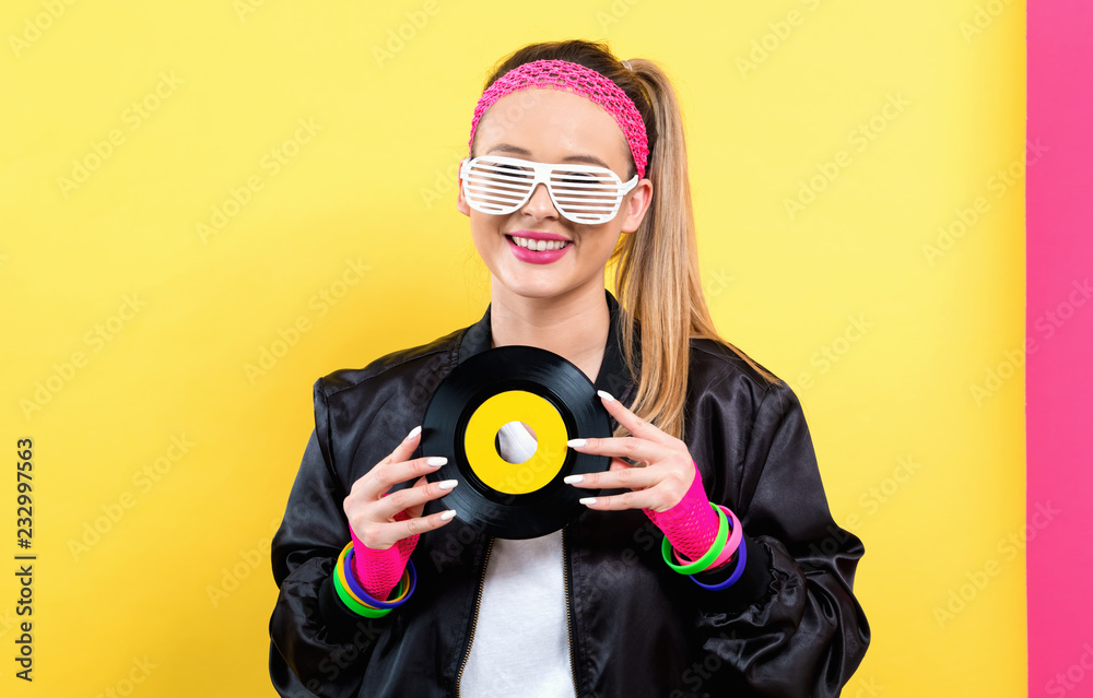 Woman in 1980s fashion holding a record on a split yellow and pink background