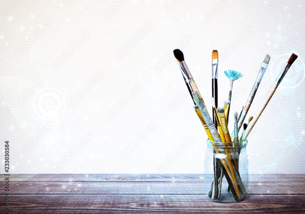 Brushes in a glass jar on the table and white wall