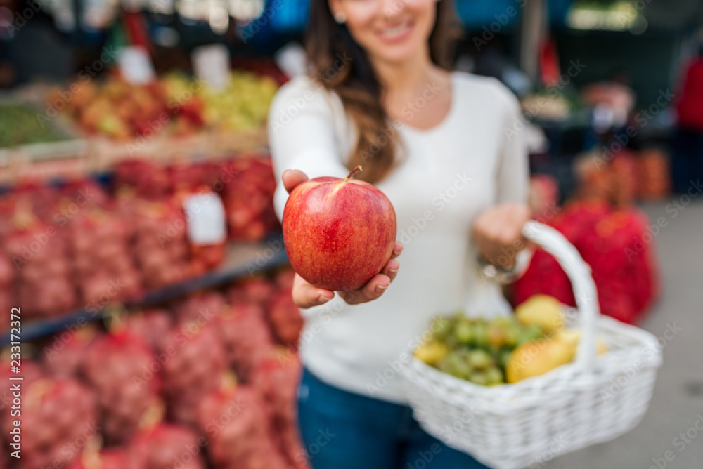 Young woman holding apple in her hand, offering. Focus on the fruit.