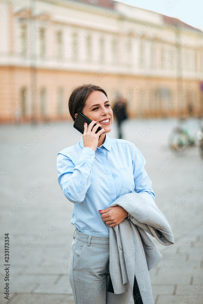 Young woman in suit talking on smartphone in the town street.