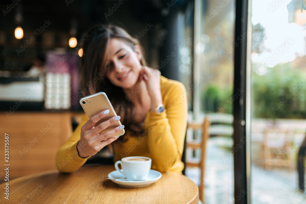 Girl using phone in the cafe. Focus on the foreground.