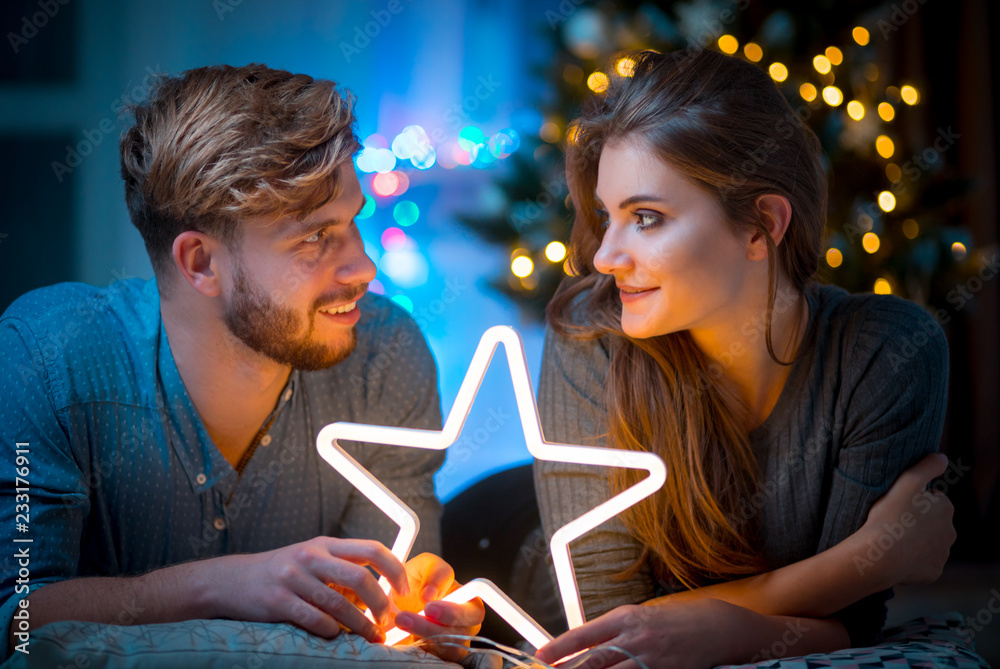 Couple in love at Christmas evening holding glowing white LED star, cozy dark living room