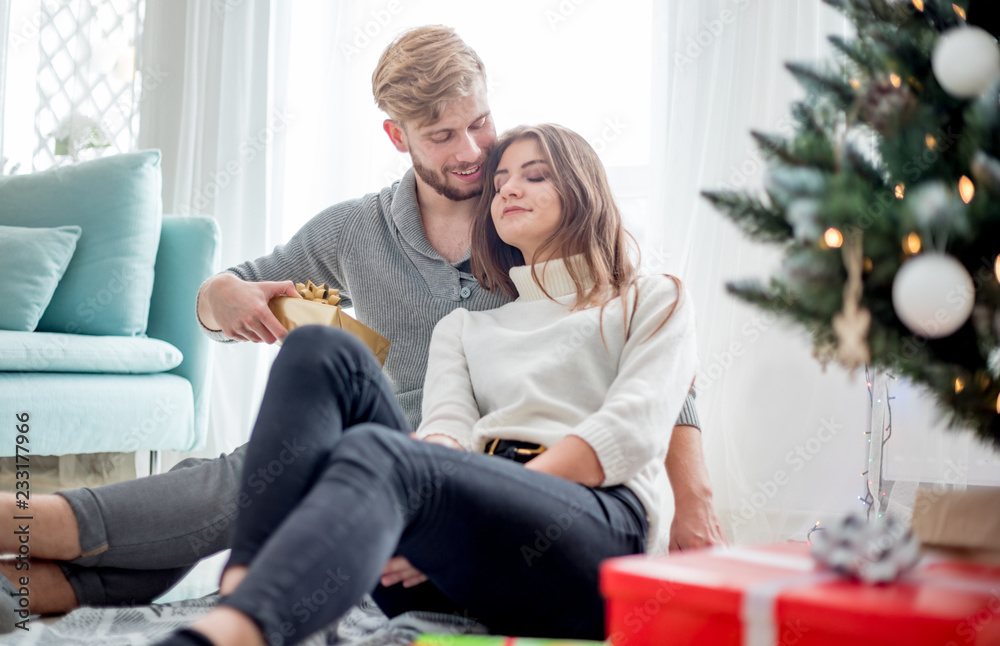 Happy couple are giving themselves Christmas gifts sitting on floor next to Xmas tree