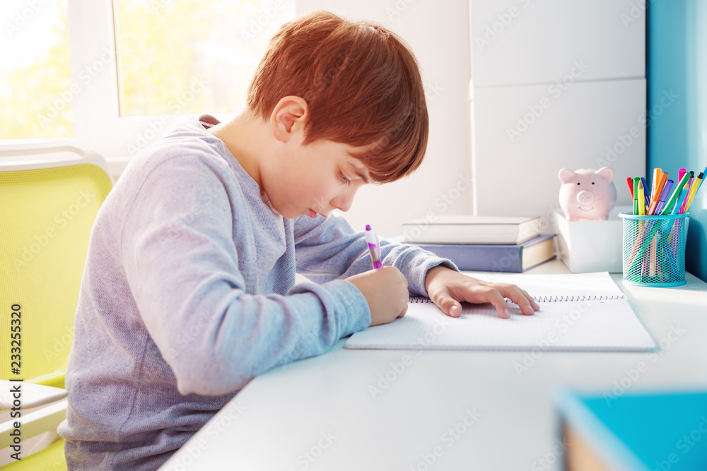 nine years old child writing at home. Boy studying at table on blue background. Kid drawing with a p