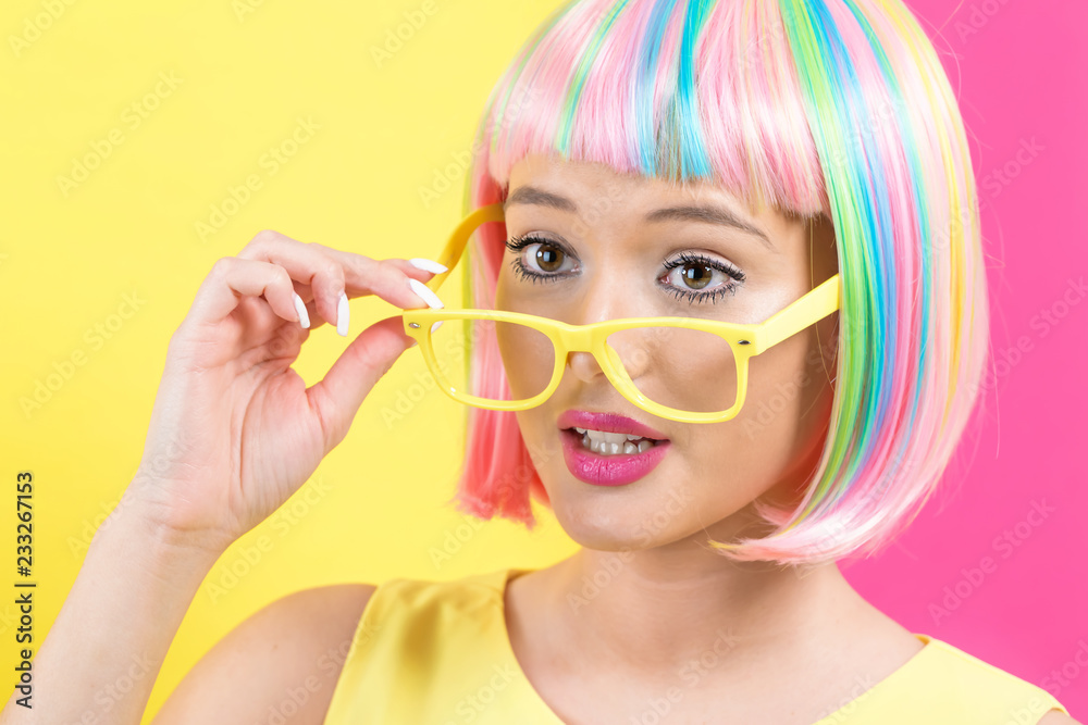 Young woman in a colorful wig with sunglasses on a split yellow and pink background