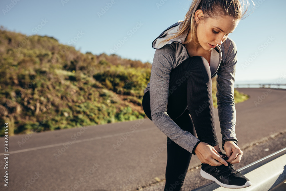 女跑步者站在路上系鞋带