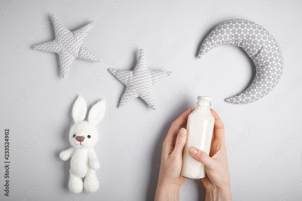 Woman with bottle of milk and toys on grey background