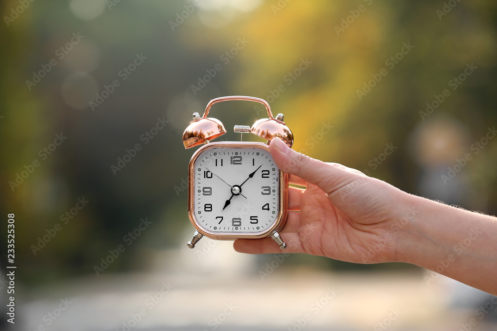 Female hand holding alarm clock on blurred background outdoors