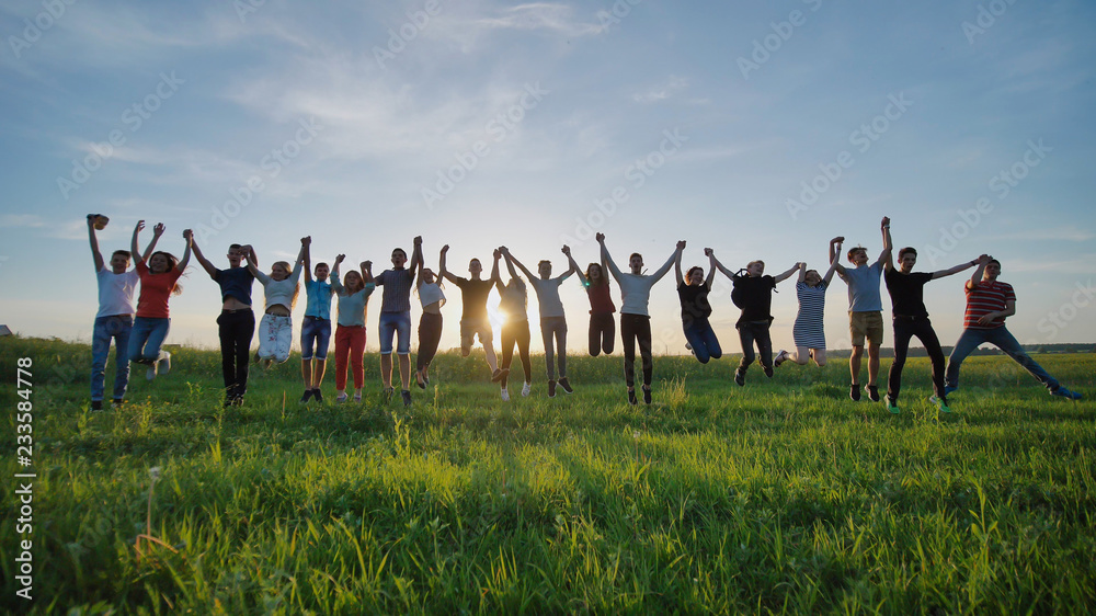 Group of best friends and students jumping outdoors. Sunset with sunshine rays.