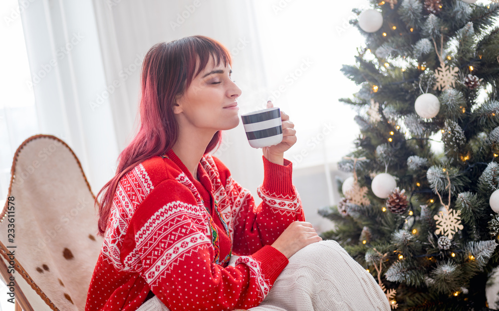 放松的美女，在圣诞树旁喝杯热咖啡或茶