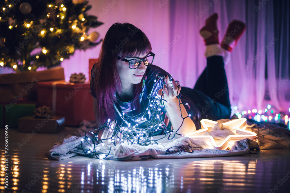 Young woman lying on floor surrounded by Christmas lights decorations at home