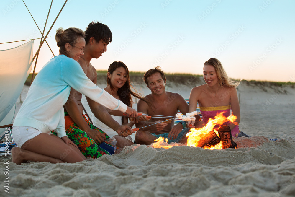 Happy friends roasting marshmallows at campfire during sunset