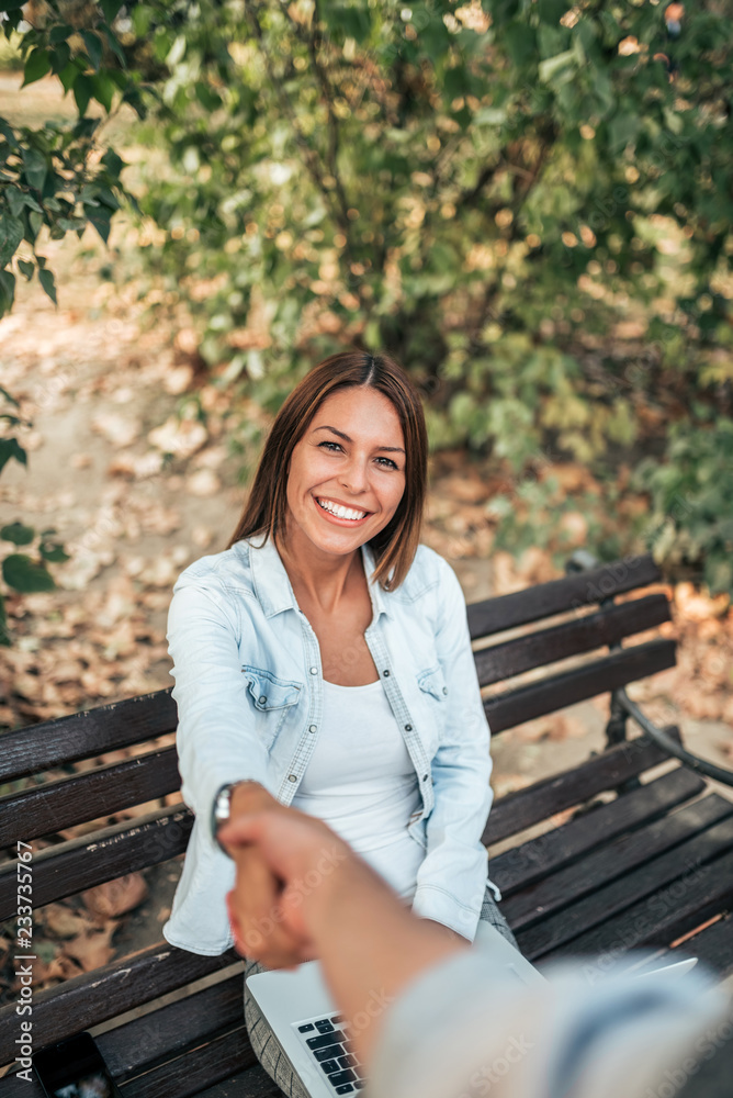 Shaking hands with a smiling young woman outdoors. POV