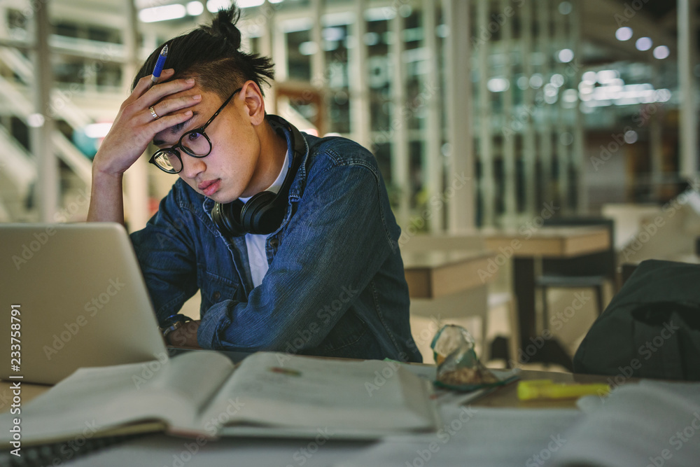 大学里沮丧的学生拿着笔记本电脑坐在图书馆