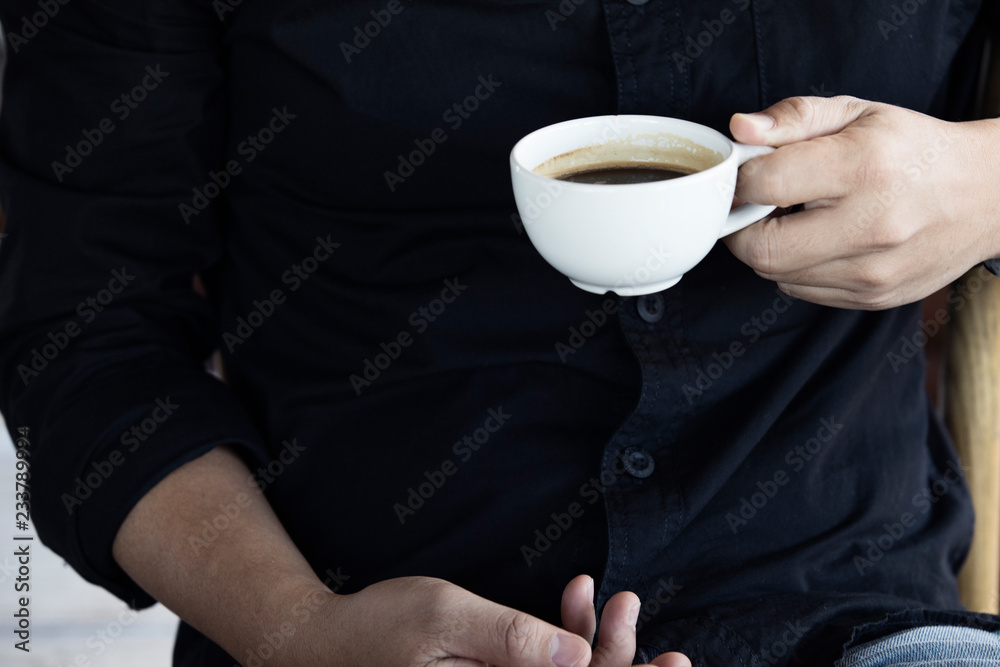 一个早上拿着一杯白咖啡的男人的手，黑色衬衫背景，特写