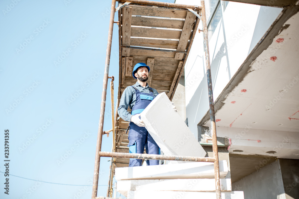 建筑工人用站在建筑脚手架上的泡沫板温暖建筑立面