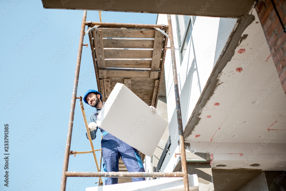 建筑工人用站在建筑脚手架上的泡沫板温暖建筑立面