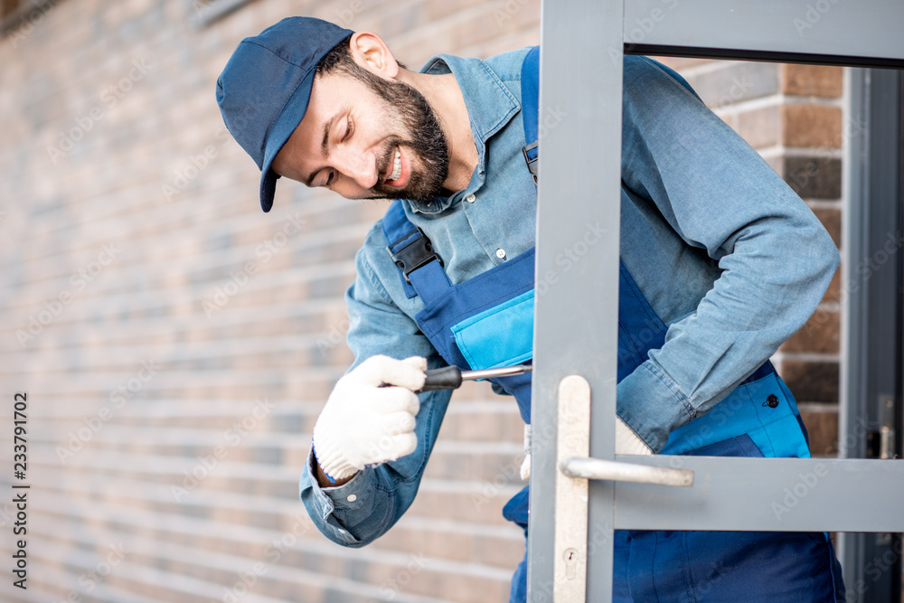 穿制服的建筑工人在室外新房子的入口门上安装门锁