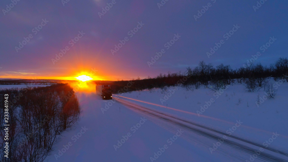 日落时分，半卡车在白雪皑皑的高速公路上行驶，沿途是森林景观