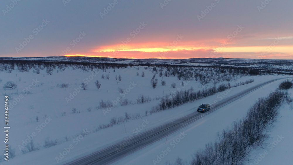 空中交通：日落时分，汽车在雪地高速公路上行驶，穿过风景如画的冬季穷乡僻壤