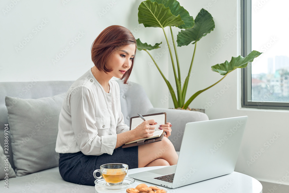 咖啡馆里的亚洲女人用笔记本电脑在记事本上记下一些数据