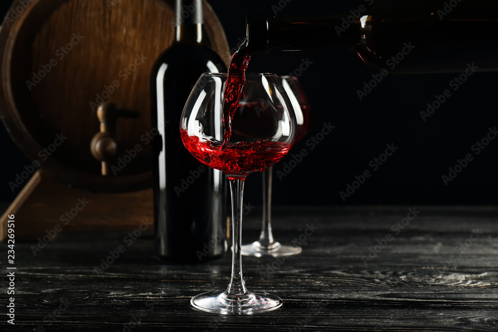 Pouring of wine from bottle into glass on dark background