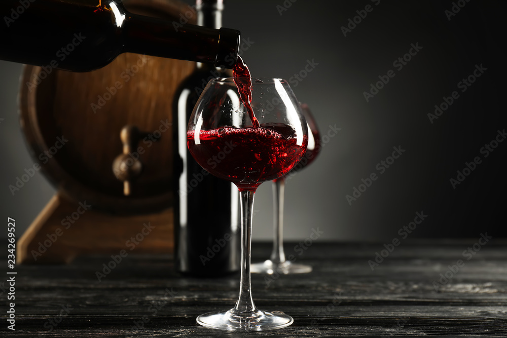 Pouring of wine from bottle into glass on dark background