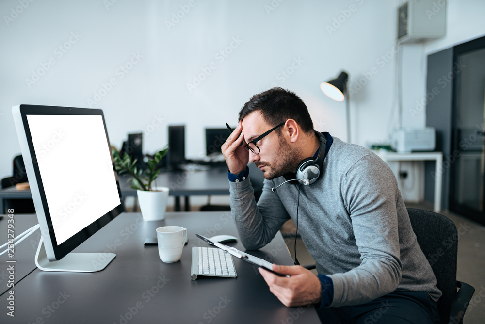 Concerned customer support agent looking at his monitor while holding files in his hand..