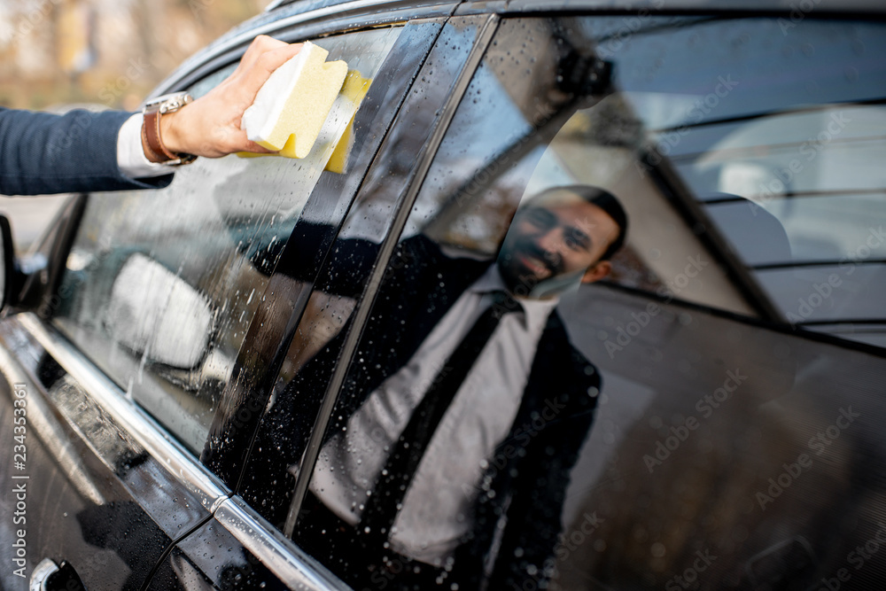 Businessman washing car window with sponge and foam on a self service car wash, close-up view with r