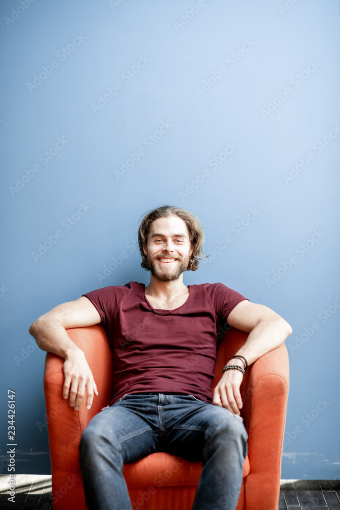 Portrait of a young caucasian bearded man with long hair dressed in t-shirt and jeans sitting on the