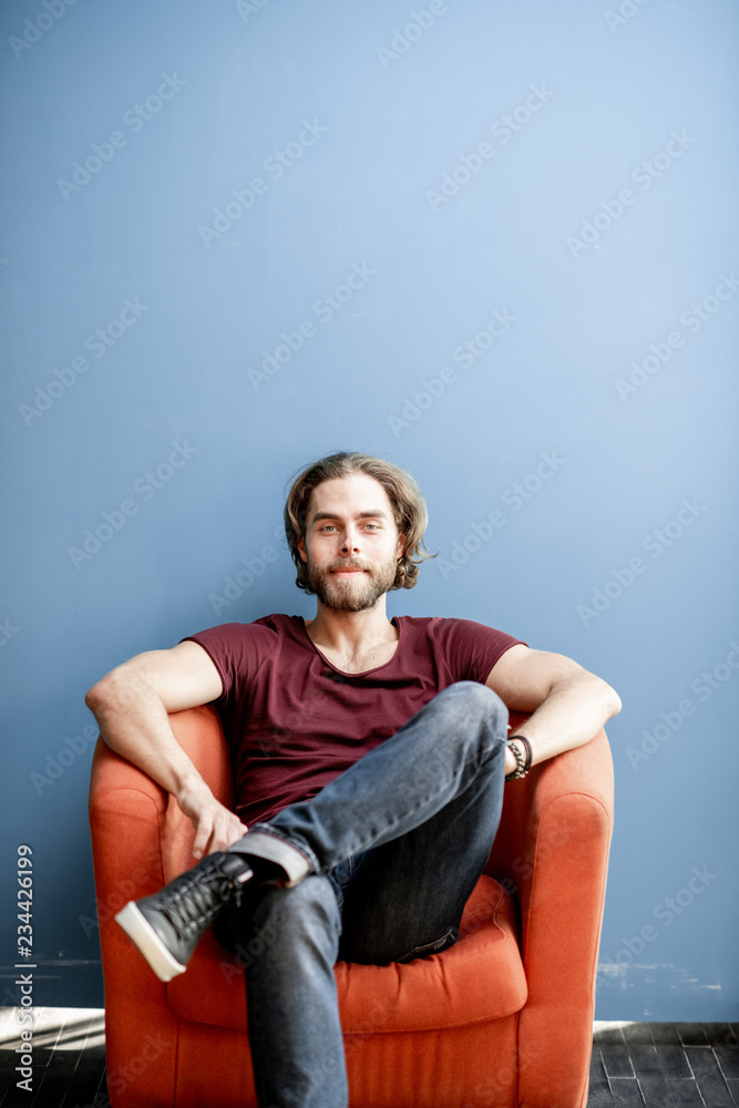 Portrait of a young caucasian bearded man with long hair dressed in t-shirt and jeans sitting on the