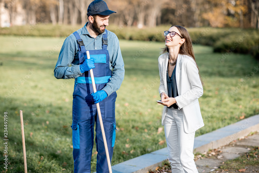 Elegant businesswoman and man sweeper in uniform talking together as old friends in the park