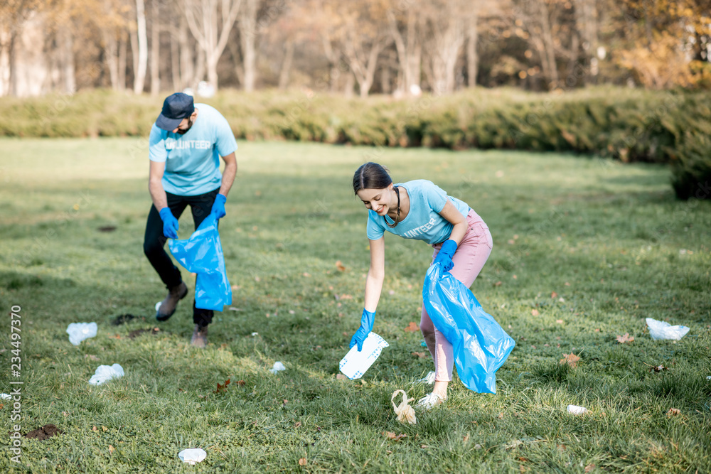 Man and woman volunteers dressed in blue t-shirts cleaning public garden from plastic rubbish into t