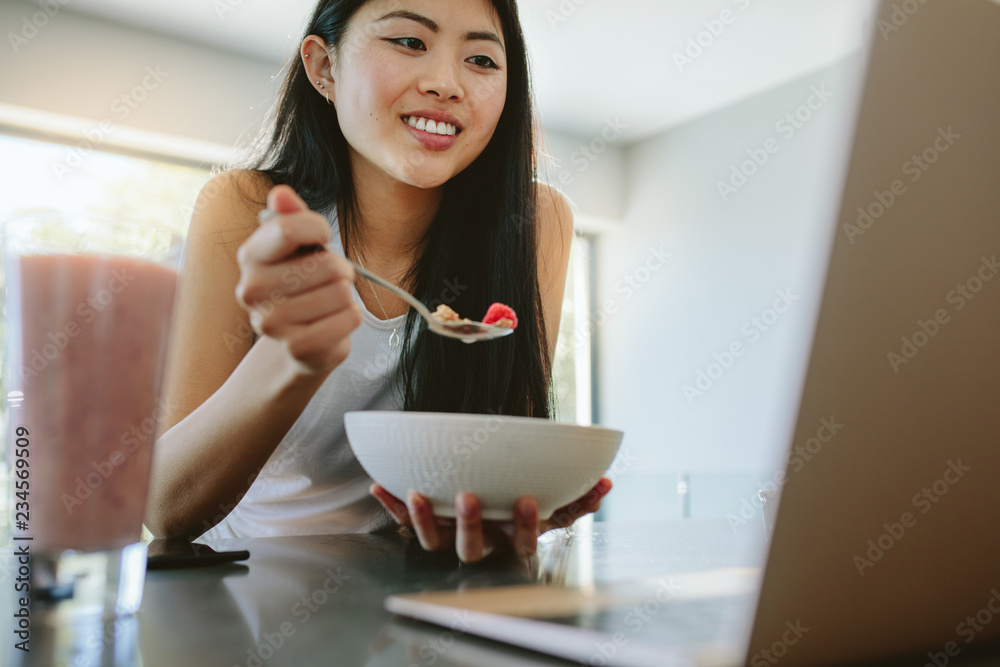 正在吃早餐并使用笔记本电脑的女人