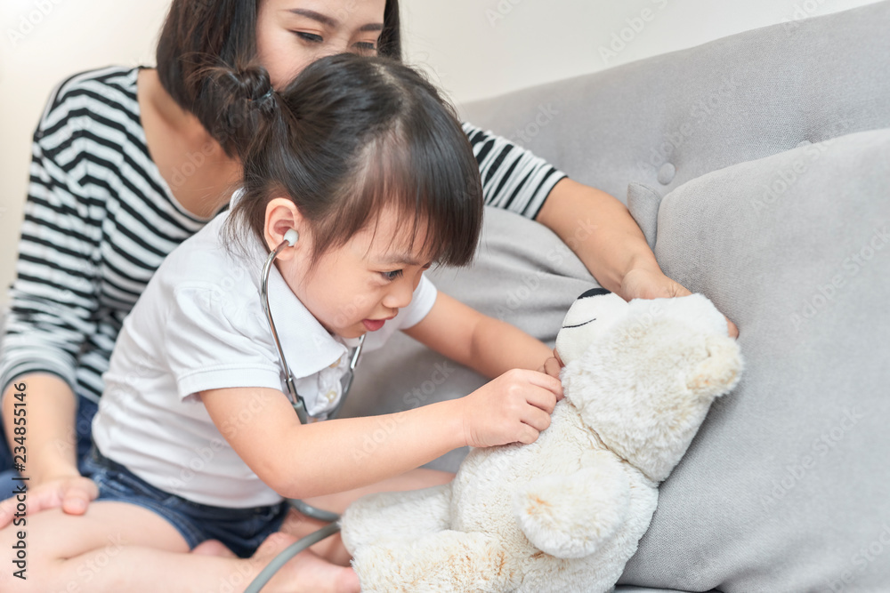 亚洲小女孩玩娃娃玩具。亚洲小女孩手里拿着听诊器检查婴儿