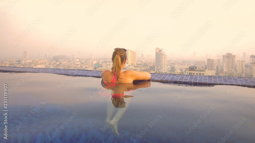 CLOSE UP: Woman enjoying a morning dip in the pool while observing the city.