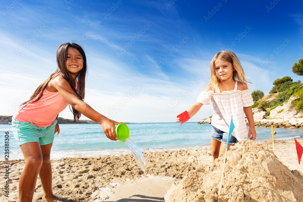 Happy girls friends building sandcastle on beach