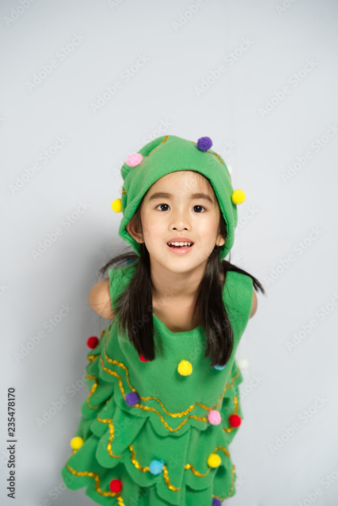 Charming little Asian girl in a christmas tree costume in a studio. Shot in isolated on white backgr