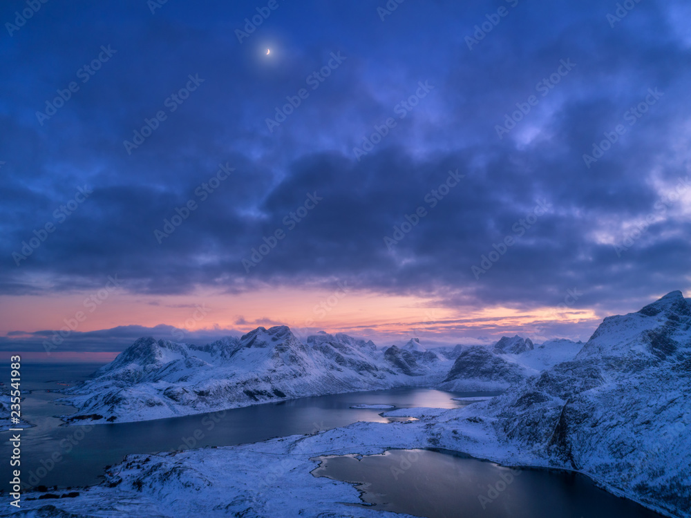 挪威罗弗敦群岛夜晚的雪山、大海和五颜六色的多云天空的鸟瞰图。冬季