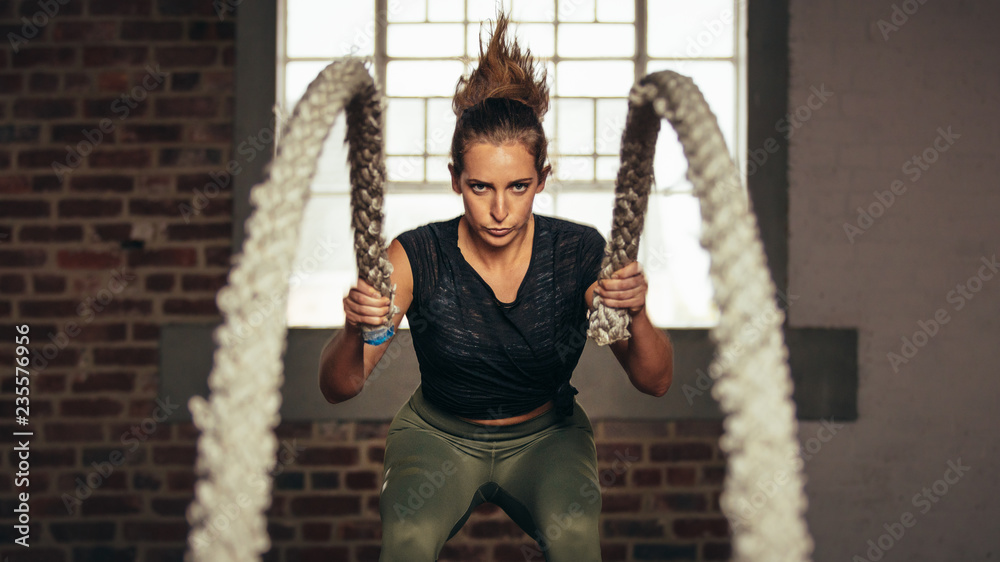 Sportswoman exercising with battling ropes at gym