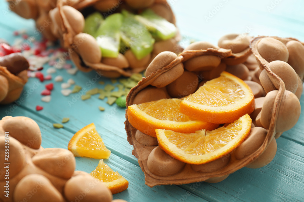 Delicious sweet bubble waffle with orange slices on color wooden table