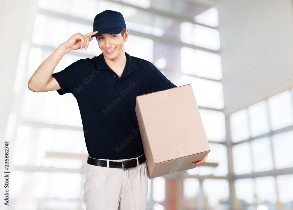 Young delivery man in black shirt and cap holding box