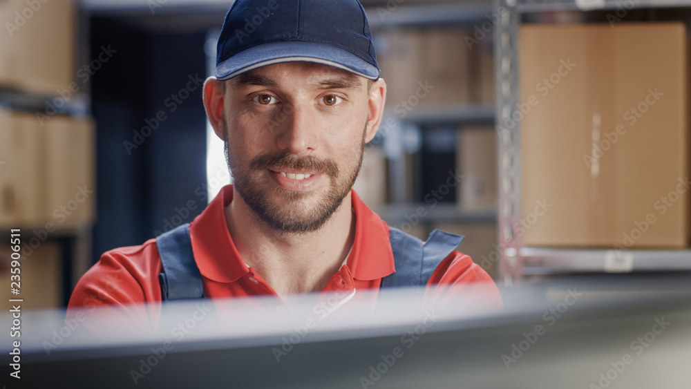 Portrait of Uniformed Worker Using Personal Computer while Sitting at His Desk in the Warehouse. 