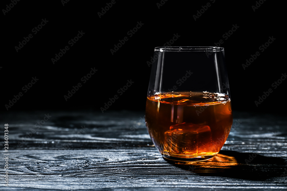 Glass of whisky with ice on wooden table against black background