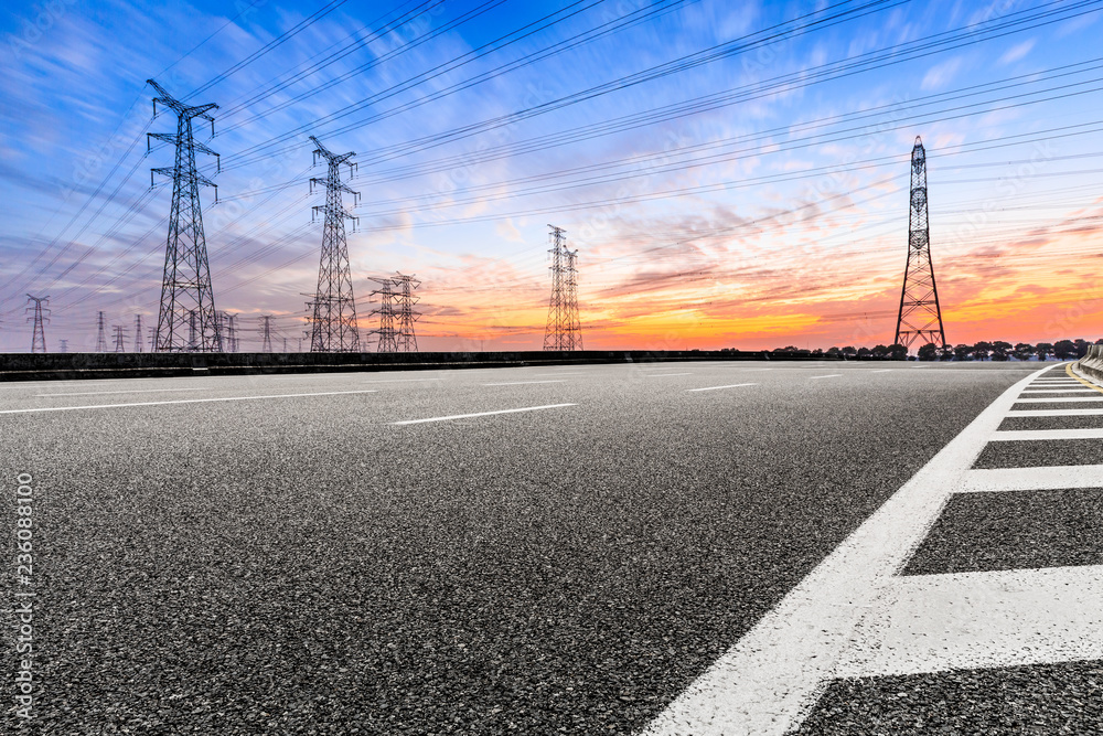 Asphalt road and high voltage power towers at sunset